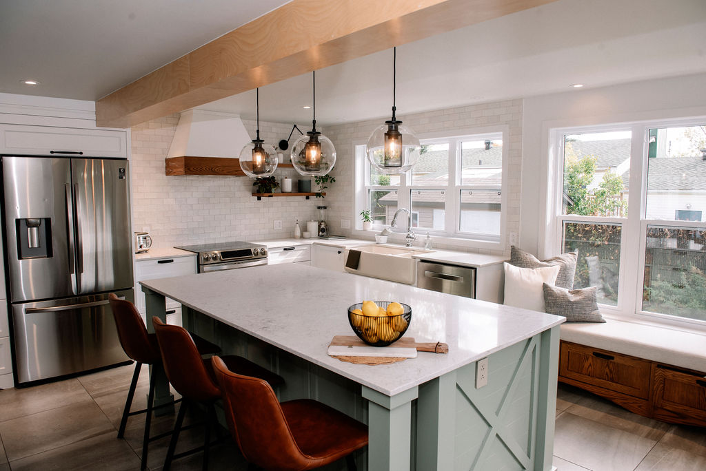 Cuisine moderne avec un grand îlot, des luminaires suspendus, des appareils électroménagers en acier inoxydable et une banquette près de la fenêtre. L'îlot est doté d'un comptoir blanc avec un bol de citrons.